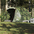Camouflage tent set up in a forested area with trees and grass.